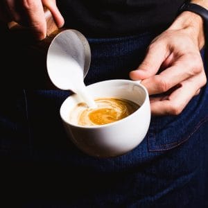 Barista pouring steamed milk to finish a cappuccino
